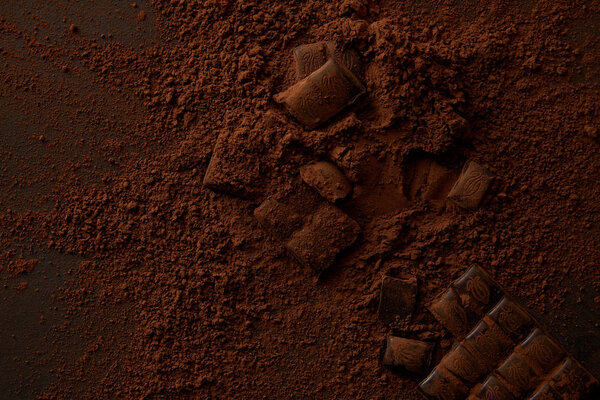 вид сверху на вкусные кусочки шоколада и изысканный какао порошок на темном фоне
 