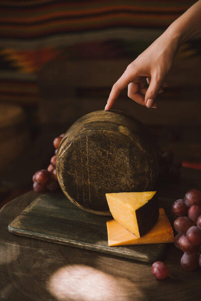 cropped shot of woman holding cheese head on cutting board with grapes
