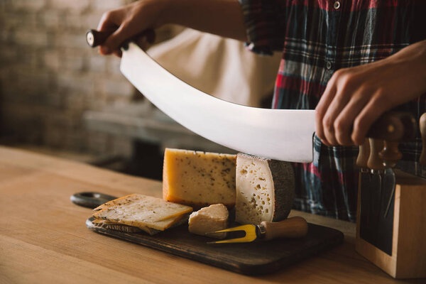 cropped shot of woman cutting delicious cheese with double handled knife