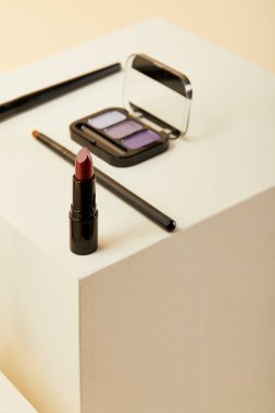 close-up shot of lipstick with purple eyeshadows case and brushes on beige clipart