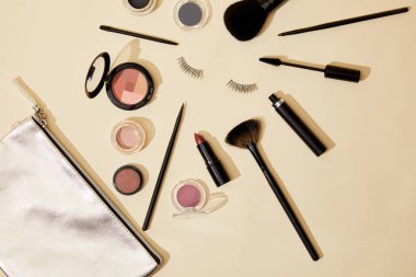 top view of various cosmetics lying on beige surface around false eyelashes clipart
