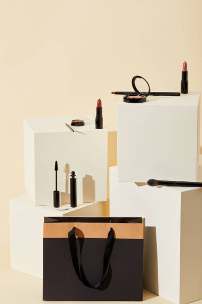 various makeup supplies lying on beige cubes with paper bag