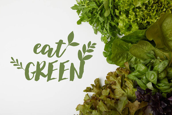 top view of fresh various leaf vegetables on white surface with "eat green" lettering