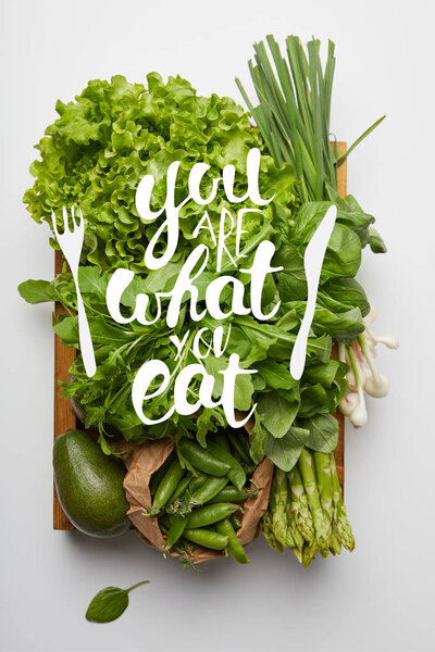 top view of various ripe vegetables in box on white surface with "you are what you eat" inspiration