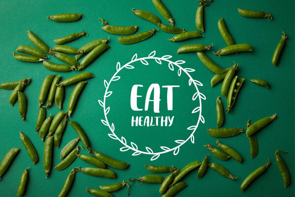 top view of round frame made of pea pods on green surface with "eat healthy" lettering