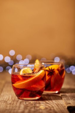 zemin üzerinde bokeh ışıkları ile ahşap yüzeyde bardaklarda portakal parçaları ve baharat ile mulled şarap görünümü kadar kapatın