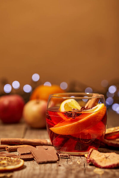 close up view of mulled wine drink, chocolate and spices on wooden surface with bokeh lights on background