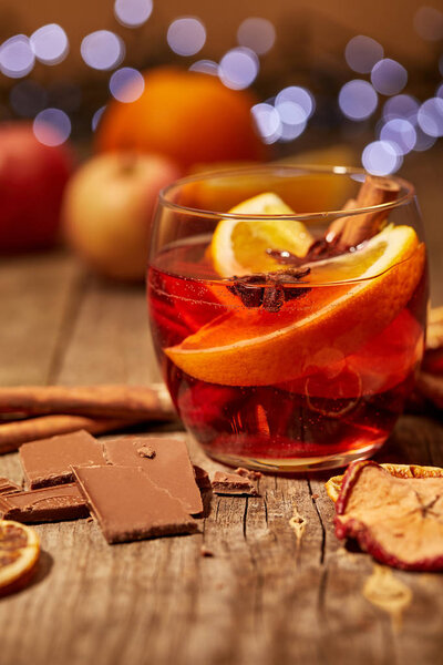 close up view of tasty mulled wine drink, chocolate and spices on wooden surface with bokeh lights on background