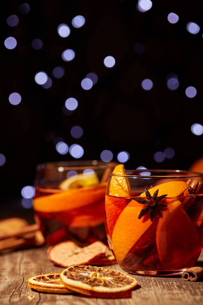 close up view of delicious hot mulled wine drinks and spices on wooden tabletop with defocused bokeh lights on background