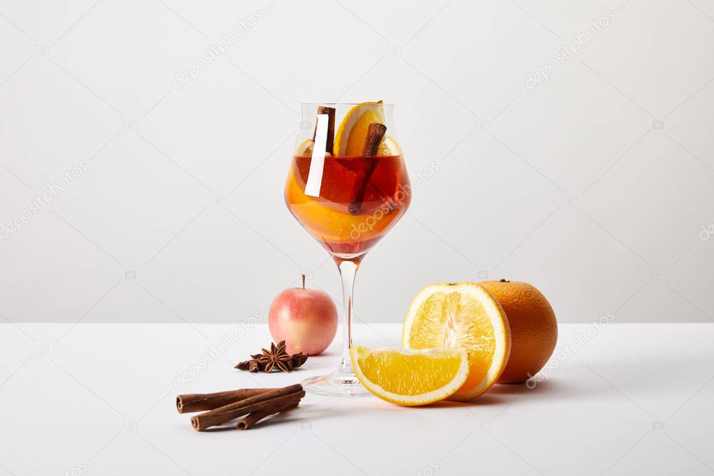 close up view of mulled wine in glass and ingredients arranged around on white tabletop on grey backdrop
