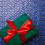 Top view of green gift with red ribbon on festive wrapping paper with stars pattern
