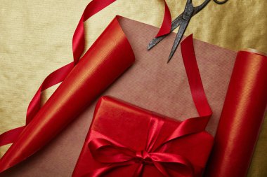 top view of scissors and christmas present with ribbon on red and golden wrapping papers background clipart