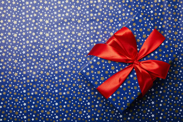 top view of wrapped gift box with red ribbon on festive wrapping paper with stars pattern