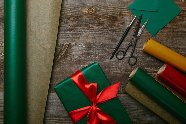 плоский укладка с завернутым рождеством подарок с лентой на деревянной поверхности с оберточной бумаги, конверт и ножницы
