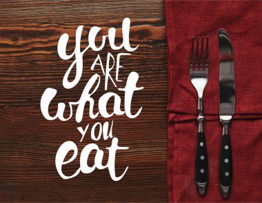 top view of fork and knife on dark red tablecloth on wooden background with 