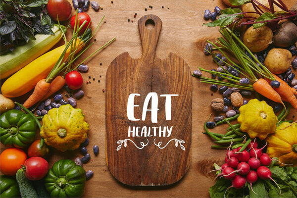Cutting board with "eat healthy" lettering and summer vegetables on wooden table