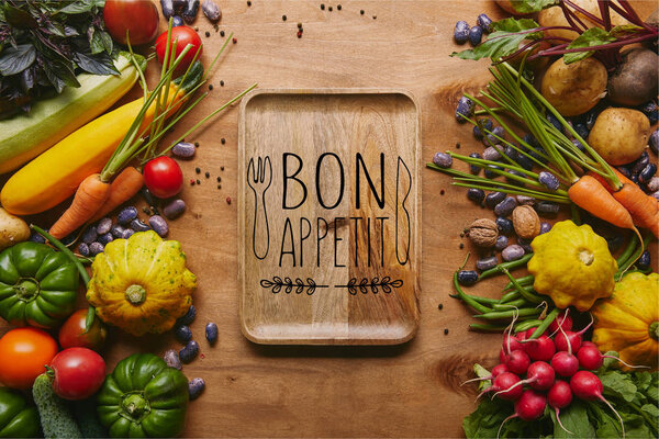 Organic raw vegetables and tray with "bon appetit" lettering on wooden table