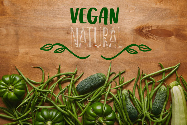 Green beans and organic vegetables on wooden table with "vegan natural" lettering