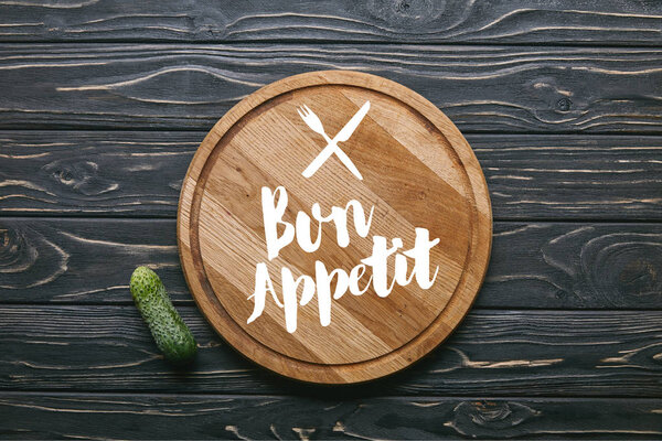 Cutting board with "bon appetit" lettering and cucumber on dark wooden table