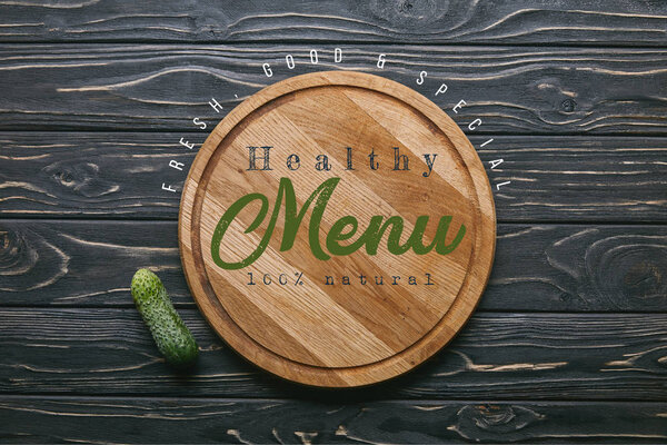 Cutting board with "healthy menu" lettering and cucumber on dark wooden table