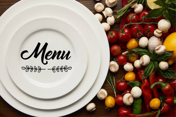 верхний вид круглых белых тарелок с надписью "меню" и свежими овощами на деревянной поверхности

