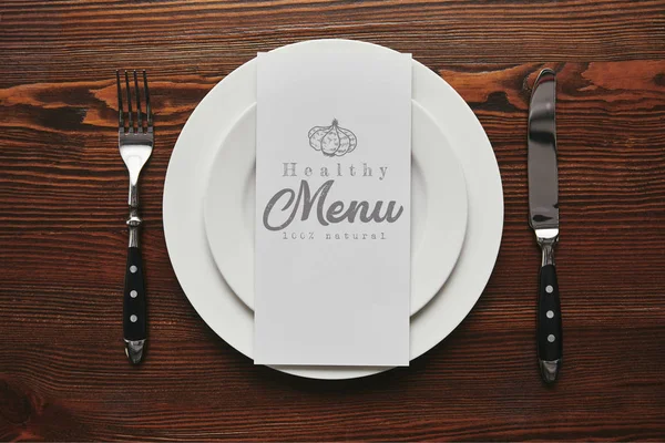 フォークで白いお皿に ヘルシー メニュー のレタリングと木製のテーブルの上にナイフとカードのトップ ビュー — ストック写真