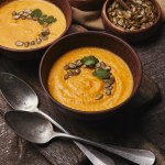 Close-up view of delicious pumpkin soup with seeds in bowls and spoons on wooden table