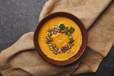 top view of tasty healthy pumpkin soup with seeds in bowl on sackcloth clipart