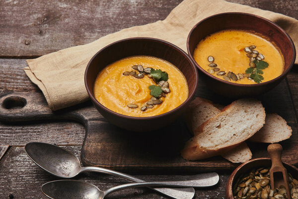 close-up view of bowls with tasty healthy pumpkin soup on wooden cutting board