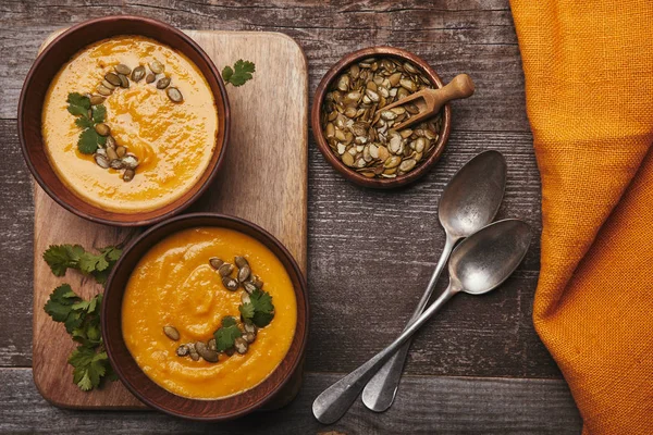 Top view of bowls with gourmet pumpkin soup, spoons and pumpkin seeds on wooden table — Stock Image Top View Bowls Gourmet Pumpkin Soup Spoons Pumpkin Seeds Wooden Stock Photo