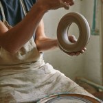 Partial view of professional potter in apron holding clay at pottery studio