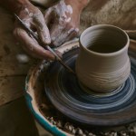 Partial view of professional potter decorating clay pot at workshop