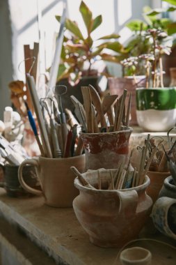 selective focus of pottery tools and paintbrushes at table in pottery studio clipart