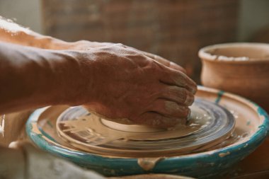 selective focus of male potter hands working on pottery wheel at workshop clipart