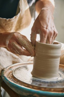 selective focus of man hands working on pottery wheel at workshop clipart