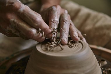 selective focus of professional potter decorating clay pot at workshop clipart