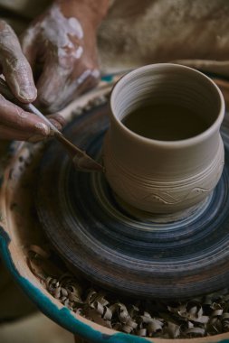 cropped image of professional potter decorating clay pot at workshop clipart