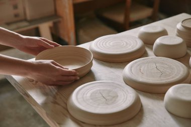 partial view of woman putting ceramic dish on table at workshop clipart