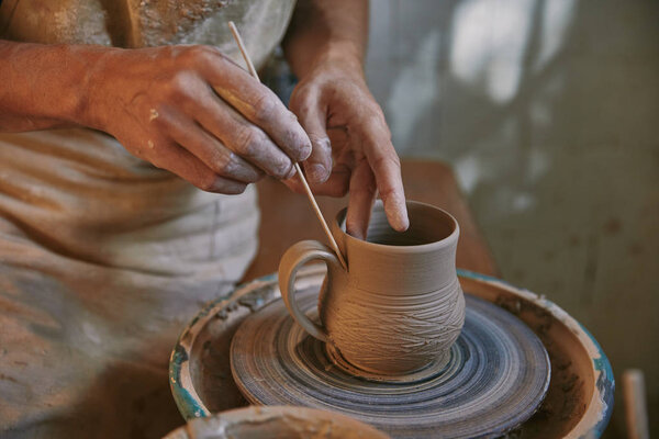 частичный обзор профессионального гончара, украшающего глиняный горшок в мастерской
