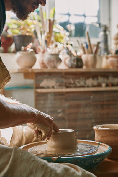 cropped image of male potter working on pottery wheel at workshop