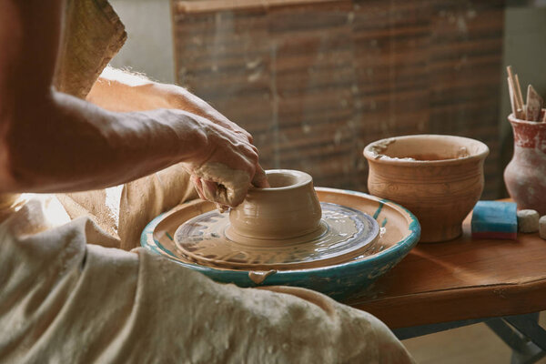 cropped image of professional potter working on pottery wheel at workshop