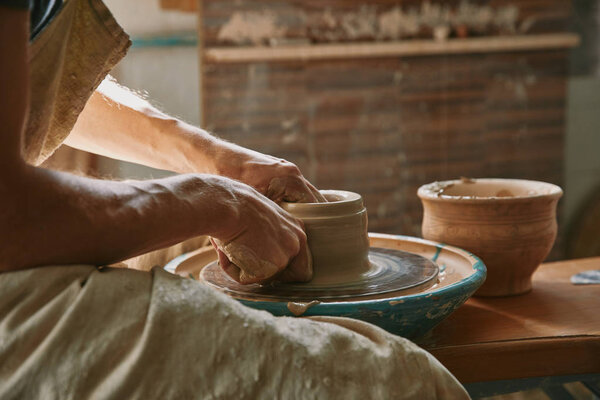 partial view of professional potter working on pottery wheel at workshop