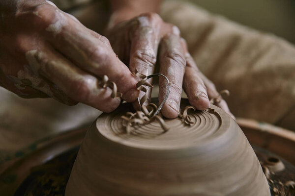 selective focus of professional potter decorating clay pot at workshop