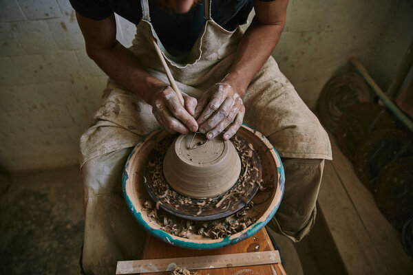 cropped image of professional potter decorating clay pot at workshop