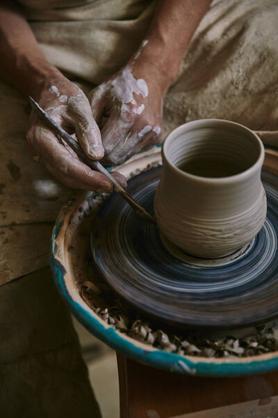 partial view of professional potter decorating clay pot at workshop
