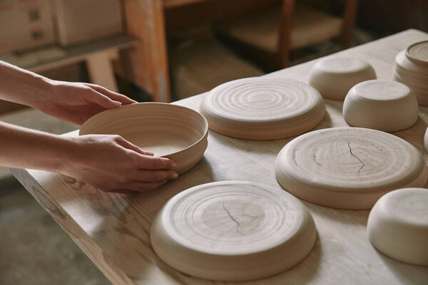 partial view of woman putting ceramic dish on table at workshop
