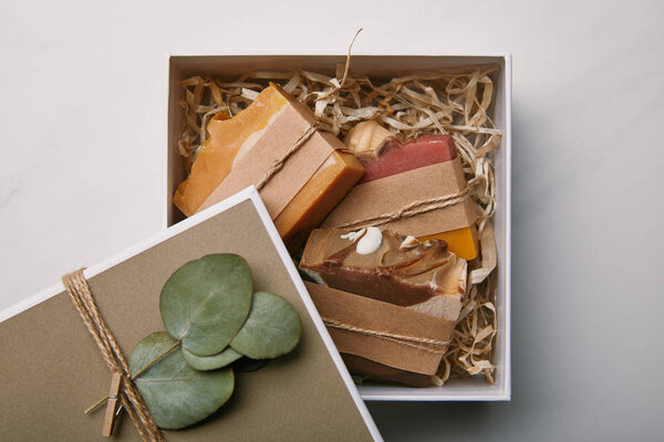 top view of box decorated with eucalyptus leaves with soap inside on white marble surface
