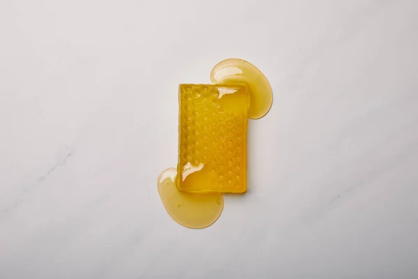 白色大理石表面用蜂蜜浇在蜂窝上的手工肥皂的顶部视图 — 图库照片