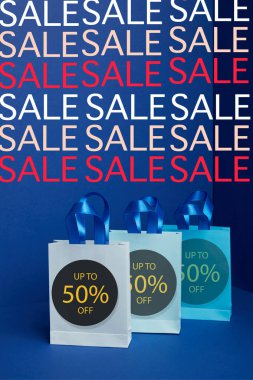 close up view of paper shopping bags arranged on blue backdrop sale signs and 50 percents discount clipart