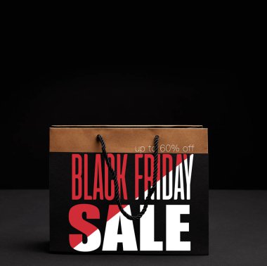 close up view of paper shopping bag on black backdrop with black friday sale and 60 percents discount